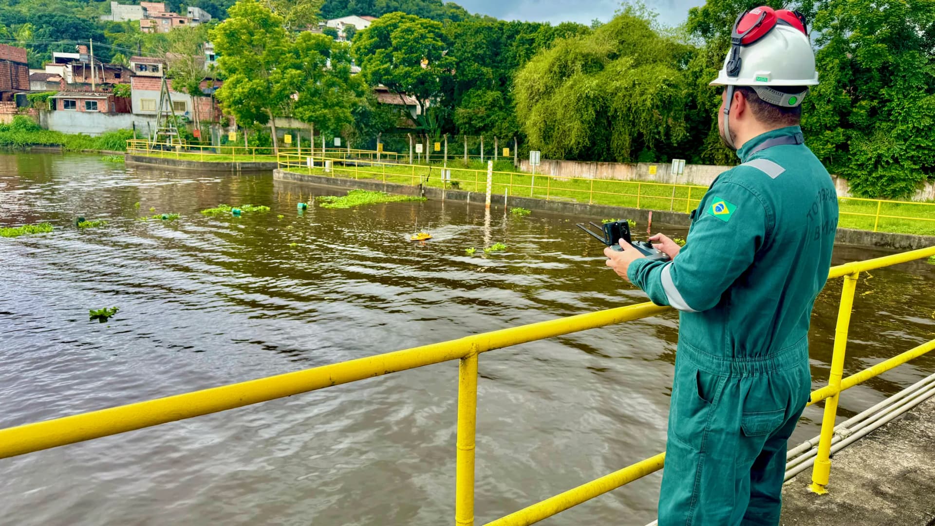 Operador BIOMAP no guarda-corpo sobre rio urbano, controlando o USV